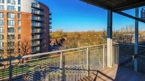 En balkong med ett metallräcke som vetter ut mot ett bostadsområde, en klar himmel och en modern byggnad med flera balkonger.