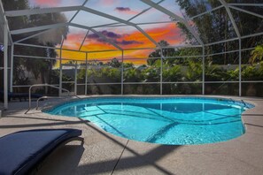 A swimming pool with a view of a sunset, surrounded by a covered area with lounge chairs. - Paradise Palms! (Siesta Key)