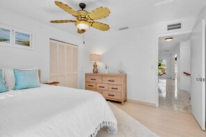A bedroom with a bed, a ceiling fan, a dresser, a lamp, and a door leading to a hallway. - Paradise Palms! (Siesta Key)