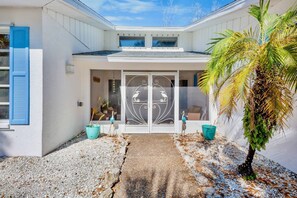 A building with a white exterior, a central entrance with a decorative door, and a small garden area with a palm tree. - Paradise Palms! (Siesta Key)