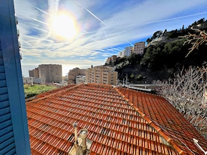 A rooftop with a traditional tiled roof, a clear sky with contrails, and buildings in the background. - Appartement 1B - MyResidenced'Azur (Beausoleil)