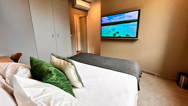 Una camera d'albergo con un letto, una televisione a muro e un condizionatore d'aria.