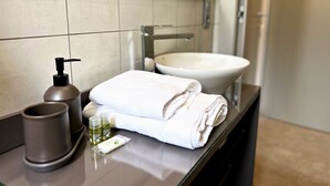 Un bagno con lavandino, specchio, asciugamano, erogatore di sapone e contenitore di vetro.