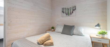 Un dormitorio con cama, mesita de noche con lámpara, planta en la pared y techo de madera.