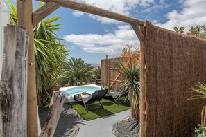 Una pérgola de madera, una piscina pequeña y una silla de descanso en un jardín.