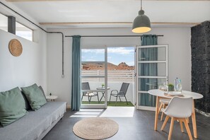 Une pièce moderne comprenant un canapé, une table à manger, des chaises, un tapis rond et une vue à travers une porte vitrée.