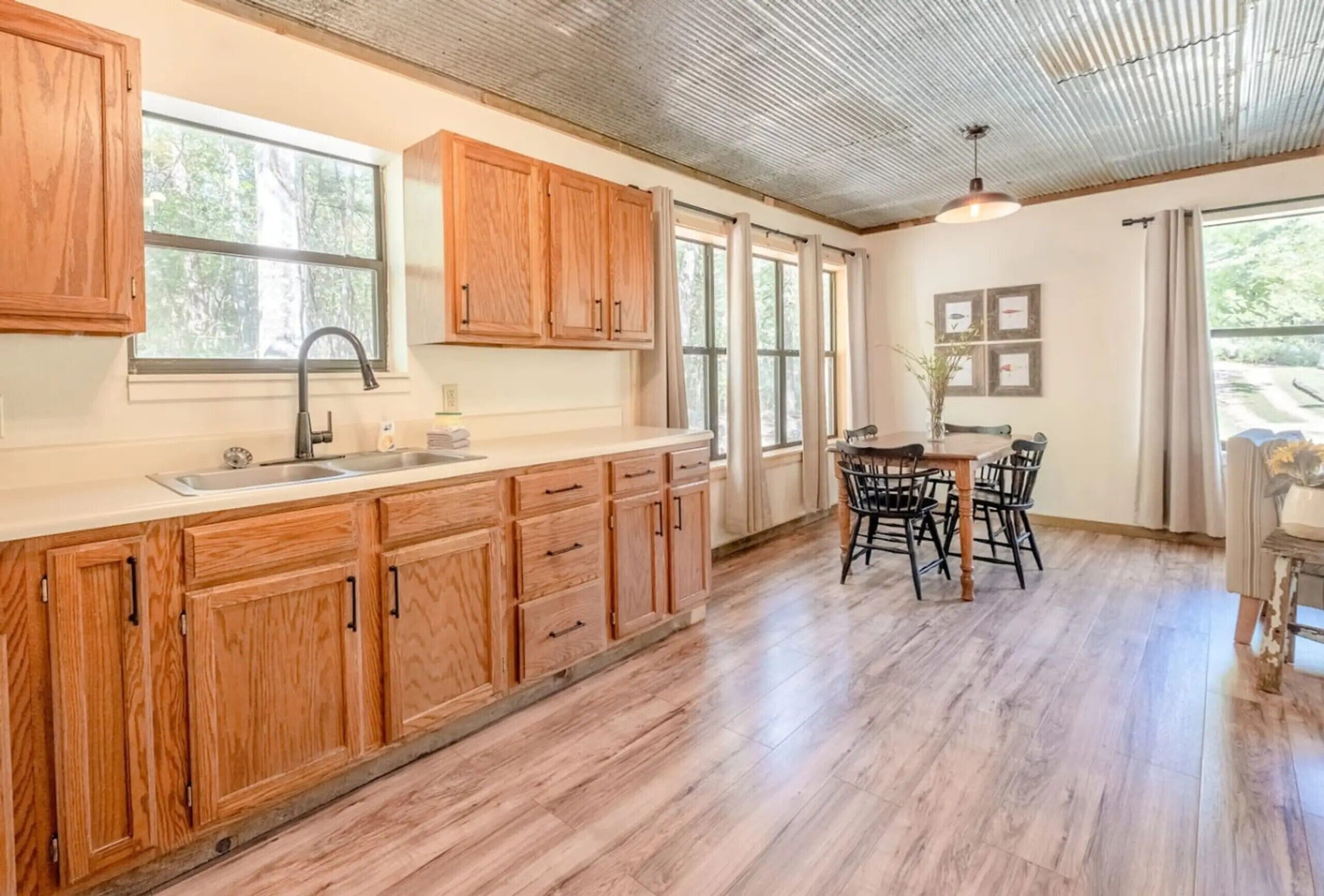 A kitchen with wooden cabinets, a sink, and a dining area with chairs.