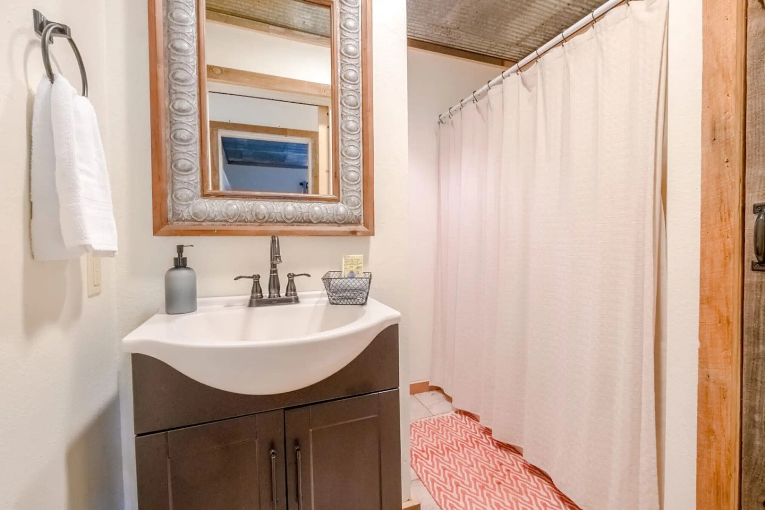 A bathroom with a sink, mirror, towel rack, and shower curtain.
