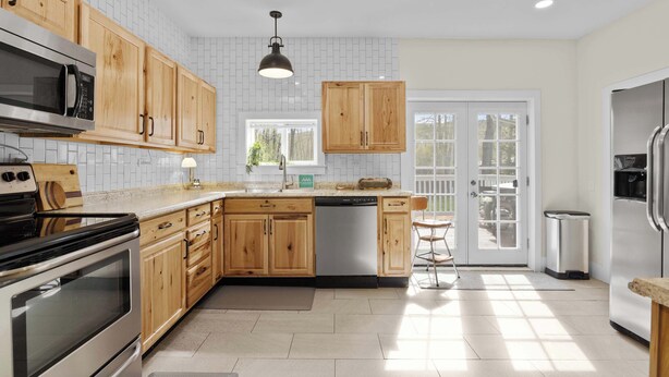 A modern kitchen with wooden cabinets, stainless steel appliances, and a large window providing natural light. - Spring Water Ranch (Red Lodge)