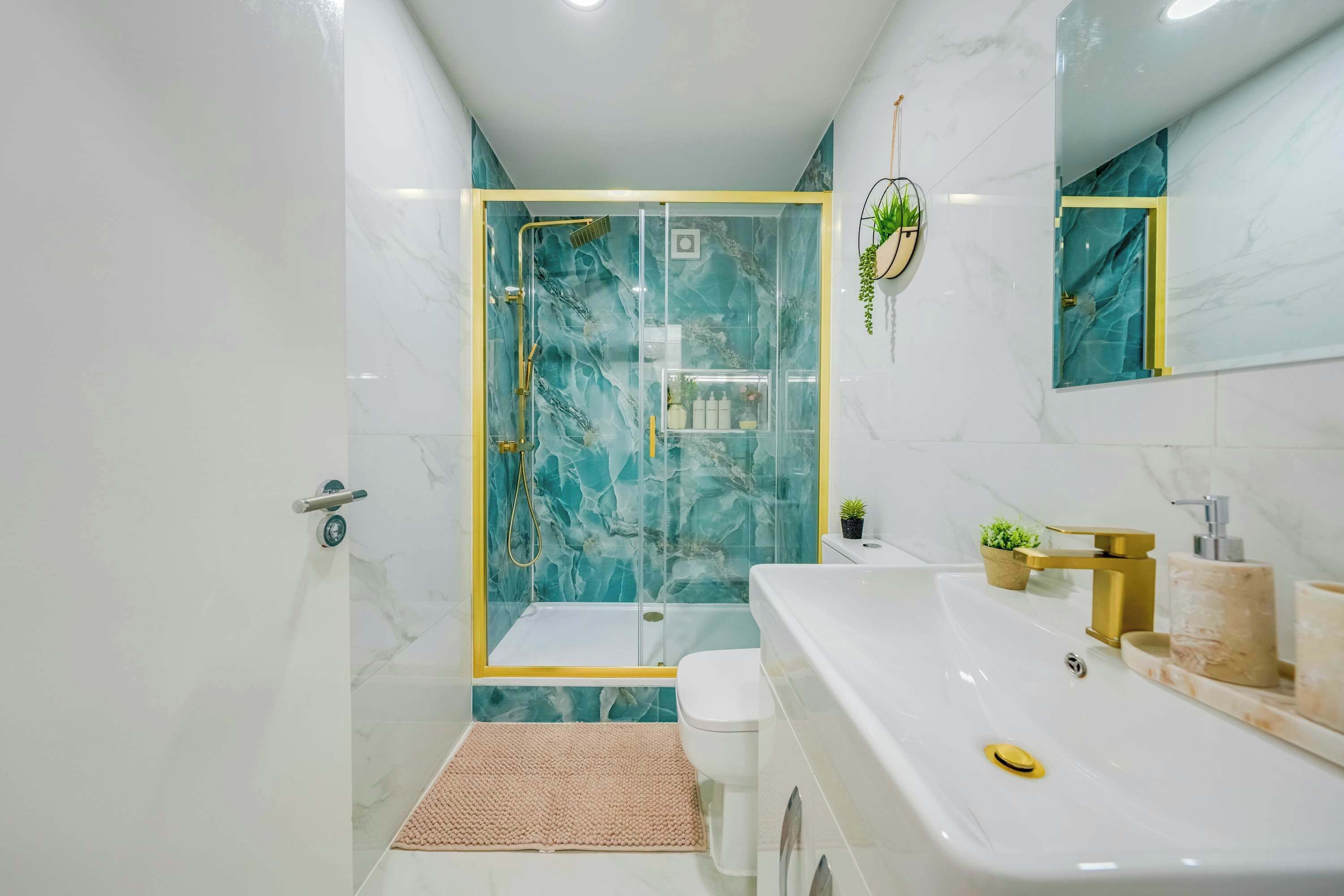 A modern bathroom with a glass-enclosed shower, a white sink with gold fixtures, and a marble-tiled floor.