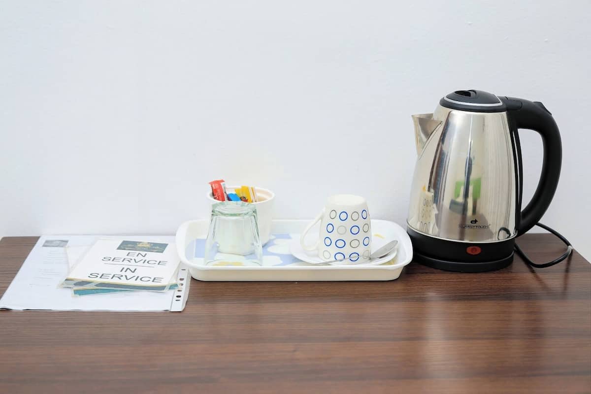 A kettle, a mug, a tray with a glass jar, and a booklet on a wooden table.