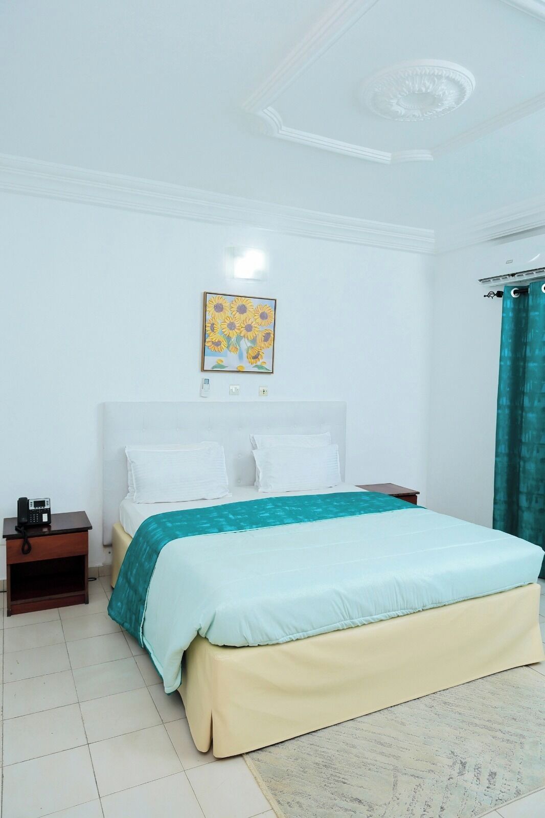 A bedroom with a bed, a nightstand, a painting, and a window with curtains.