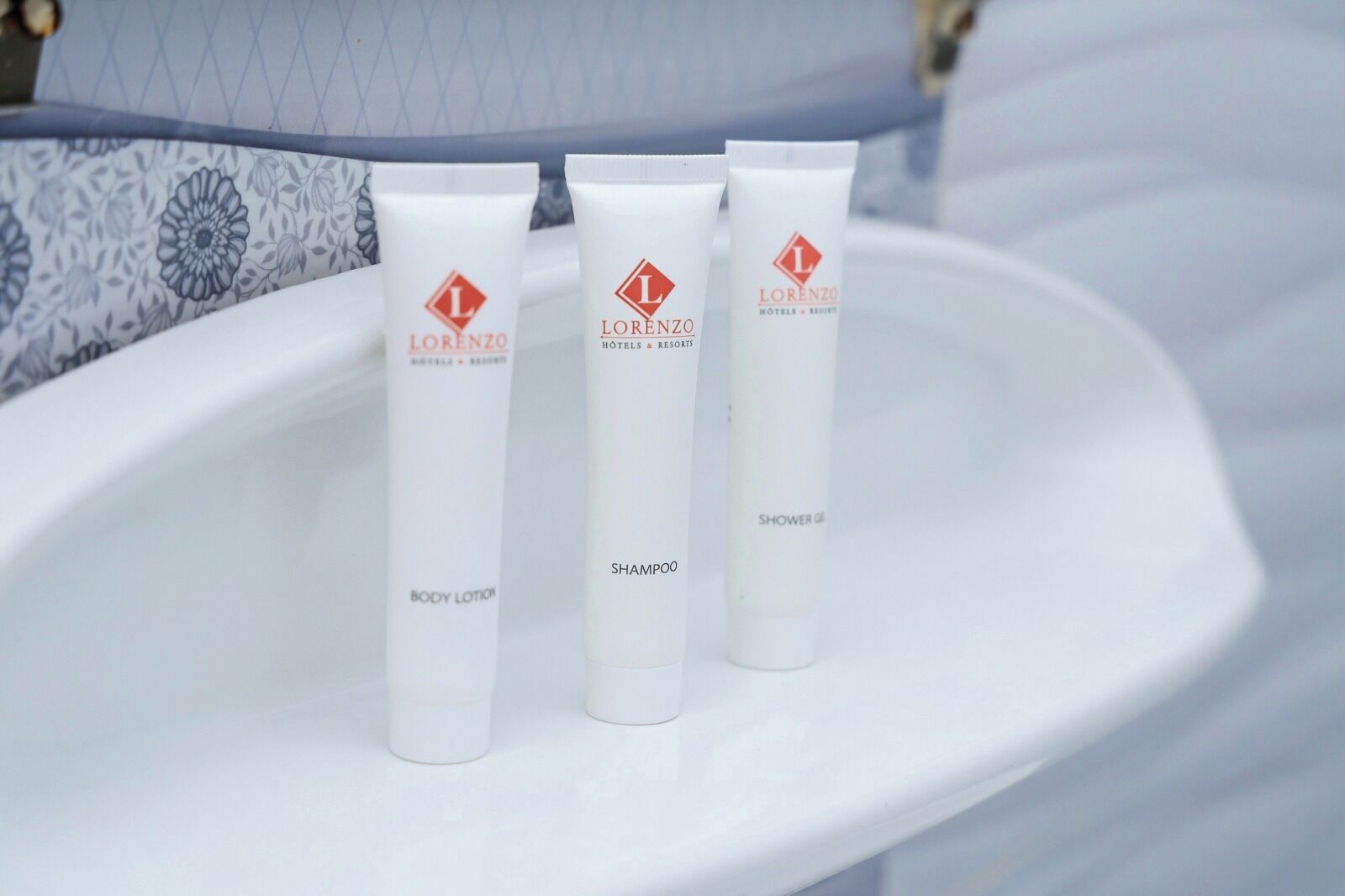 Three white tubes of body lotion and shampoo on a white bathroom sink.