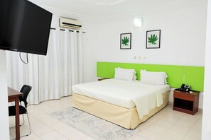 Una habitación de hotel con cama, escritorio, silla, aire acondicionado, televisor y dos cuadros con hojas en la pared.