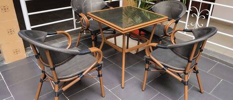 A set of four wicker chairs with a glass-top table on a tiled patio.
