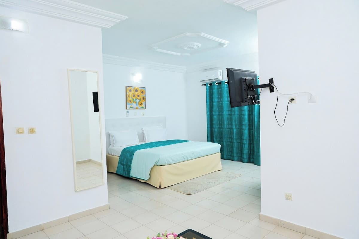 A bedroom with a bed, a TV mounted on the wall, and a window with curtains.