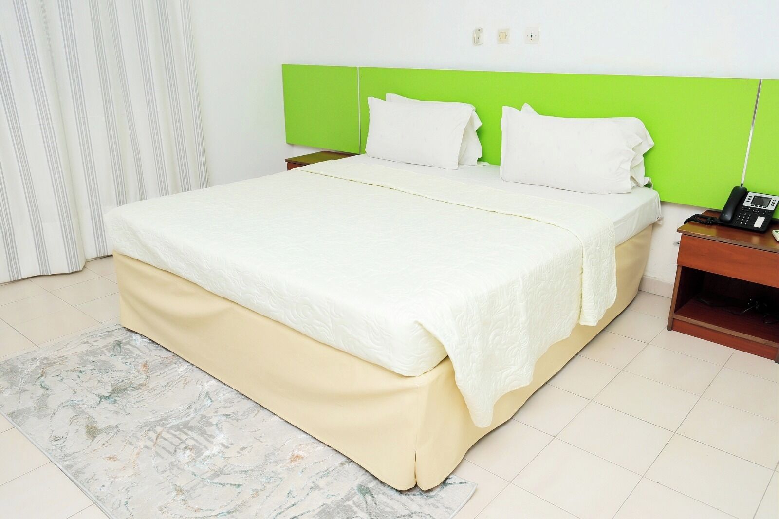 A bed with a green headboard, white bedding, and a bedside table with a phone.