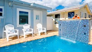 Ein Swimmingpool mit zwei weißen Liegestühlen, einer gefliesten Poolanlage und einem Gebäude mit einer Uhr und einem Rettungsring.