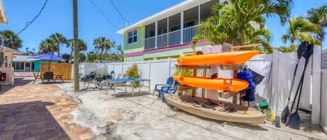 Una propiedad frente al mar con un porche cubierto, mobiliario exterior y un bote con kayaks y chalecos salvavidas.
