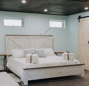 Un dormitorio con una cama de madera, dos ventanas, una lámpara de techo y una puerta.