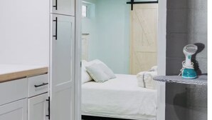 A room with a bed, a white wardrobe, a small shelf with a toothbrush, and a door leading to another room.