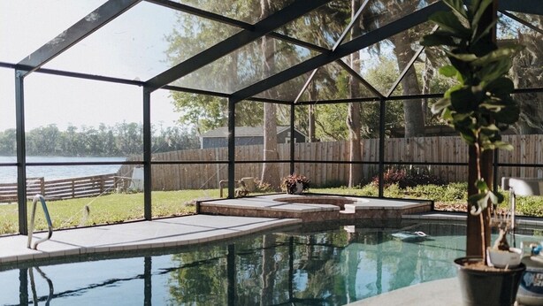 A swimming pool with a glass enclosure, surrounded by a wooden deck and a grassy area.