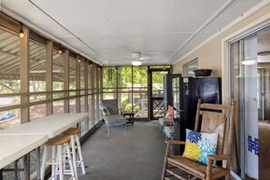 Un patio techado con mesa y sillas, un ventilador de techo y vistas al exterior.