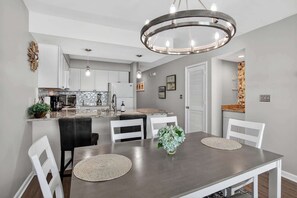 A modern kitchen with white cabinets, a dining area with a round table and chairs, and a chandelier. - Oceanfront Delight 2BR 2Ba Views Pool N Myrtle (North Myrtle Beach)