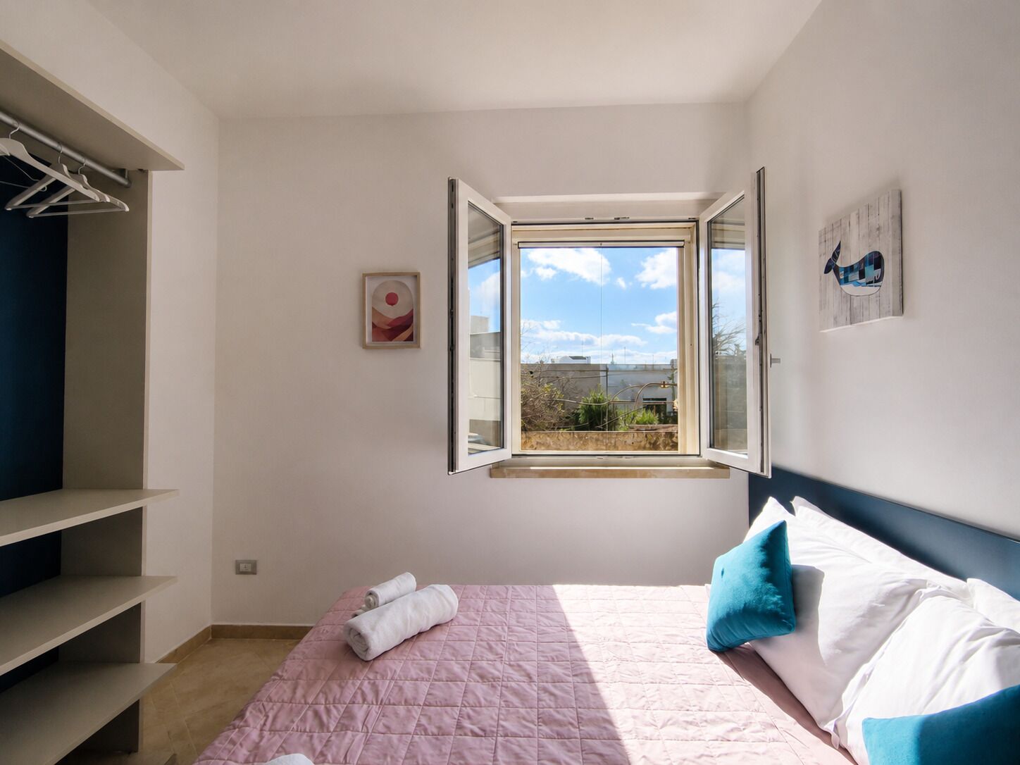 A bedroom with a bed, a window, a wardrobe, and a painting.