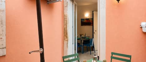 Un pequeño patio con una mesa dispuesta para dos personas, sillas, una lámpara fijada a la pared y un equipo de aire acondicionado.