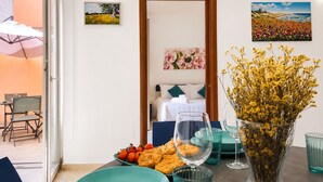 Une pièce avec un lit, une table à manger dressée, un vase rempli de fleurs et un tableau accroché au mur.