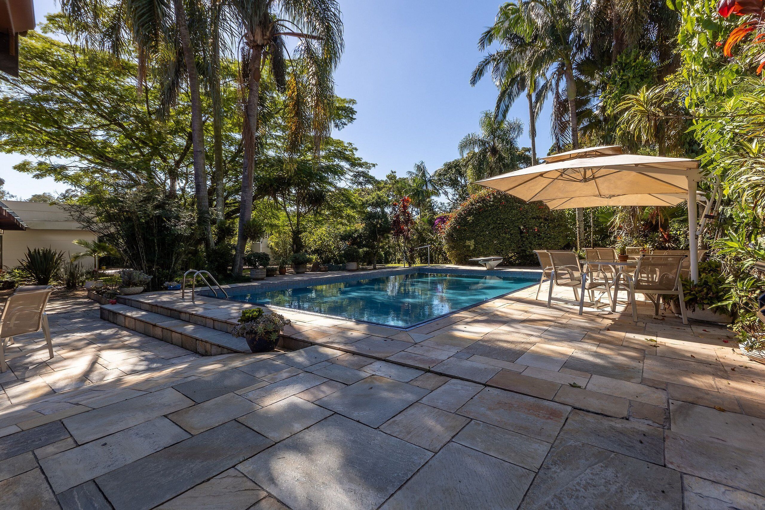 A swimming pool with steps, surrounded by stone tiles, and shaded by a canopy.