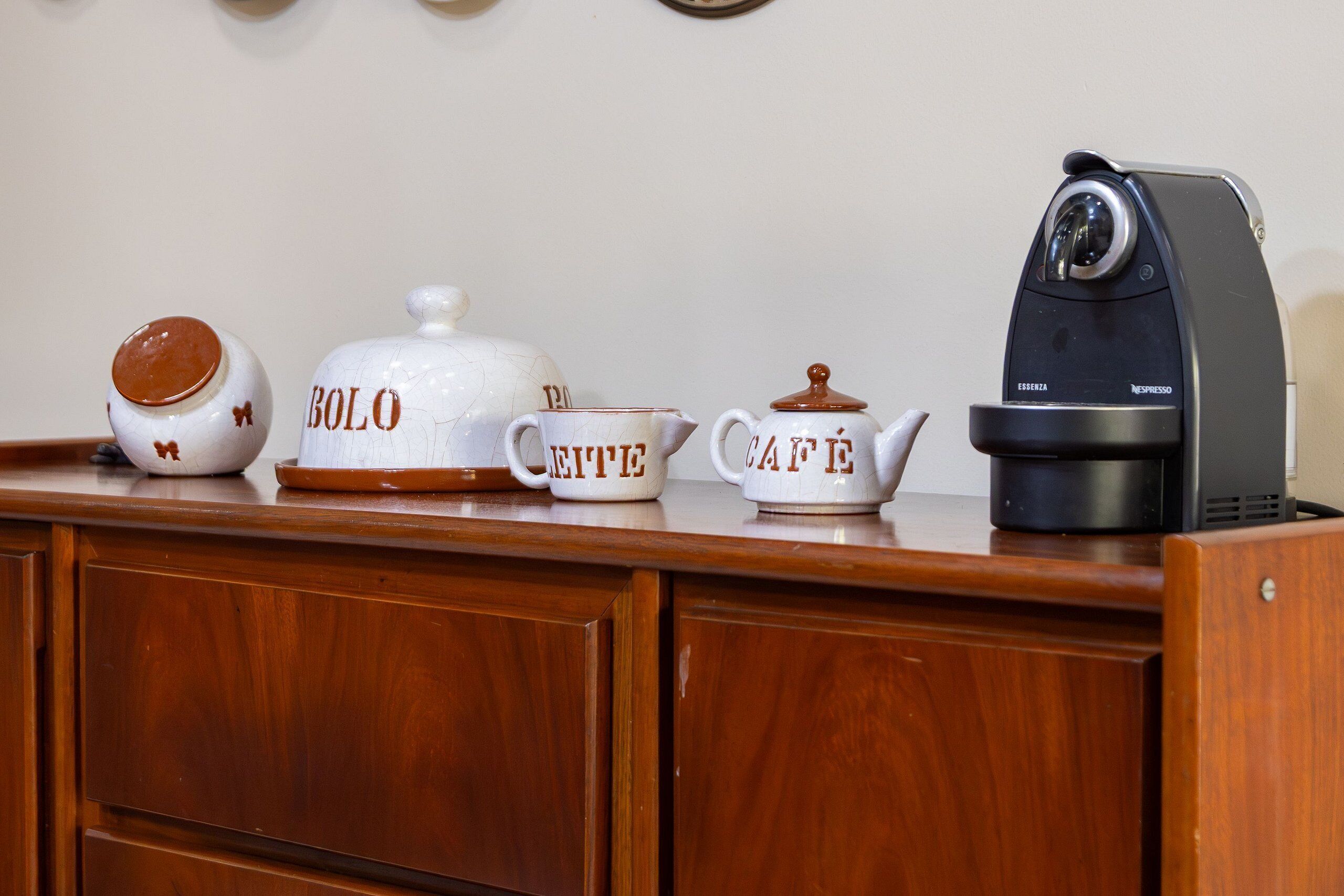 Un bancone cucina con una macchina da caffè, tre caffettiere in ceramica e un pensile in legno.