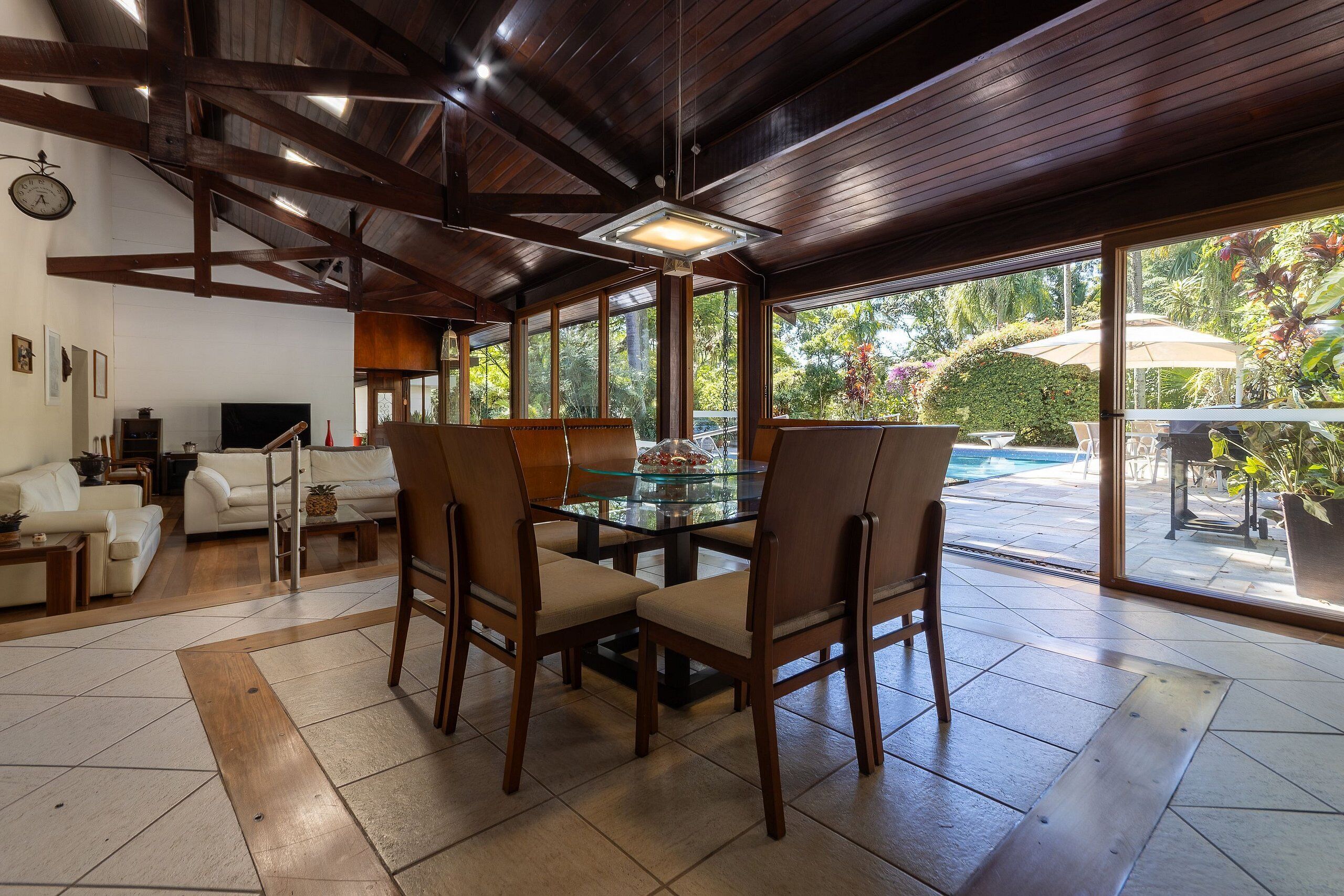 A spacious living area with a glass dining table, wooden chairs, and a large window offering a view of the outdoors.