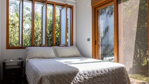 Un dormitorio con una cama grande, una mesita de noche, una ventana con persianas y un ventanal corredero que da a un balcón.