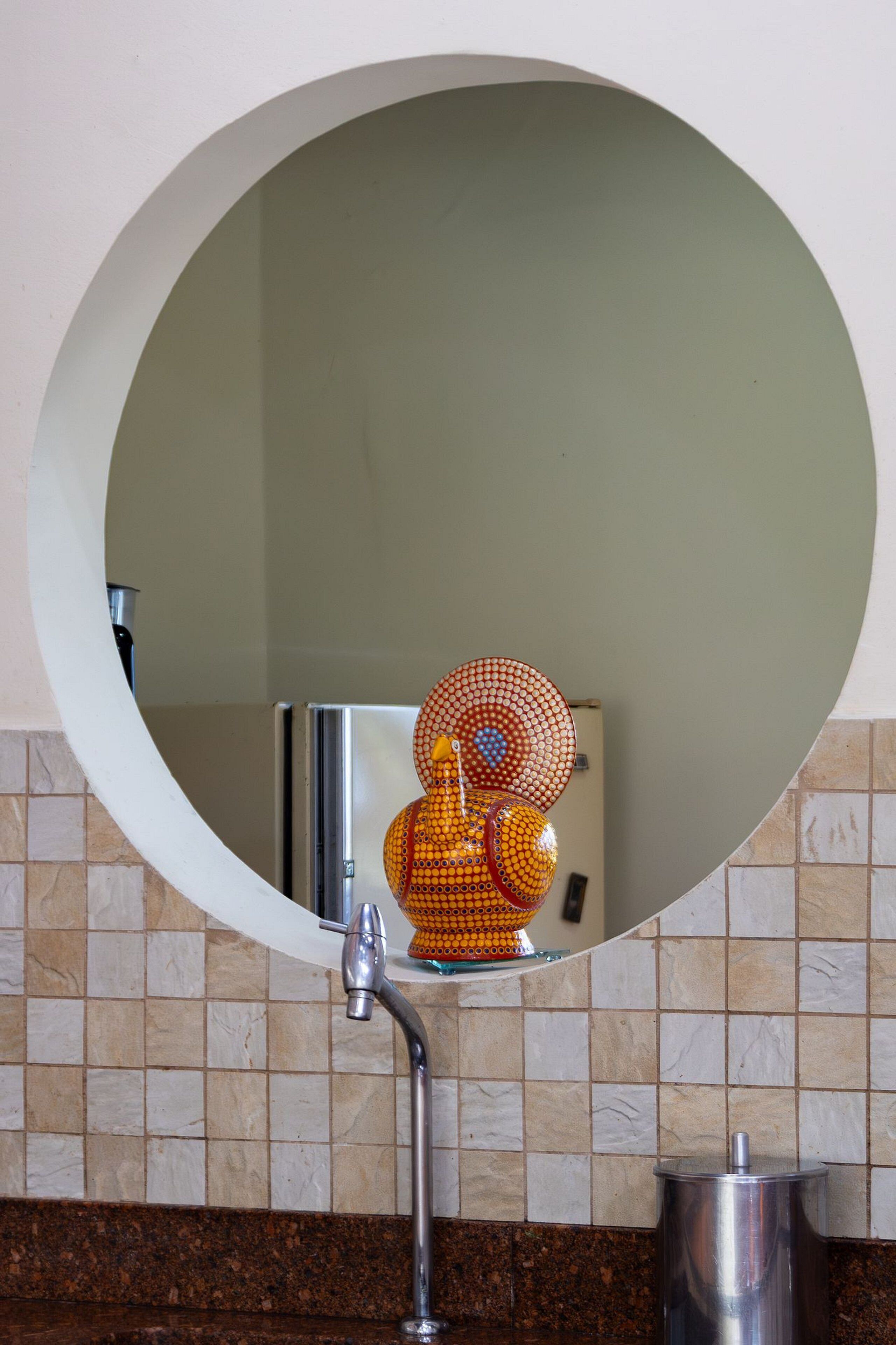 Casa de banho com espelho redondo, lavatório e objeto decorativo laranja e amarelo.