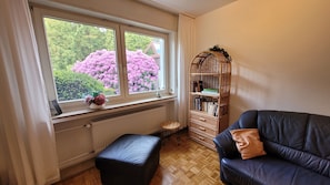 Una habitación con ventana, radiador, estantería, sofá de cuero y un taburete pequeño.