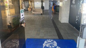 Een hotelgang met een receptiebalie, een blauw tapijt met een logo en een bord dat de richting naar de lift aangeeft.