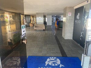 A hotel corridor with a reception desk, a blue carpet with a logo, and a sign indicating the direction to the elevator. - Sand, Sun and Sea - Apart-Service Ondina / Salvador (Salvador)