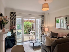 A living room with a sofa, a glass coffee table, a lamp, a mirror, and a view of the garden through a glass door. - Charming 2 bed house in Pinner (Pinner)