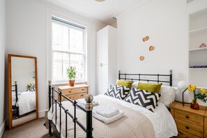 Ein Schlafzimmer mit Bett, Nachttisch, Kommode, Fenster und Spiegel.
