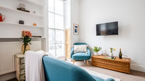 A modern living room with a sofa, a blue armchair, a wooden sideboard, a television, and a bookshelf. - Chic 1 bed apartment Near British Museum (London)