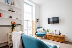 Ein modernes Wohnzimmer mit einer Couch, einem blauen Sessel, einer Holzkommode, einem Fernseher und einem Bücherregal.