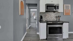 Una cocina moderna con armarios blancos, un microondas de acero inoxidable y un salpicadero de azulejos.