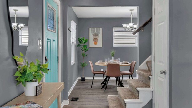 Un pasillo con una recepción, un comedor con mesa y sillas, una escalera y una planta en maceta.