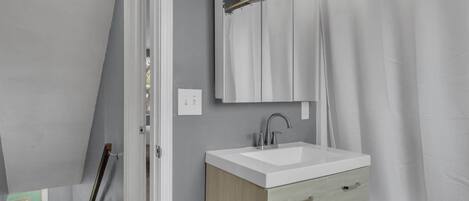Un baño con lavamanos blanco, un espejo y una cortina de ducha.