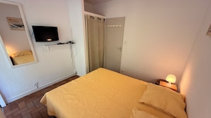 A bedroom with a bed, a television mounted on the wall, a door, and a nightstand with a lamp.