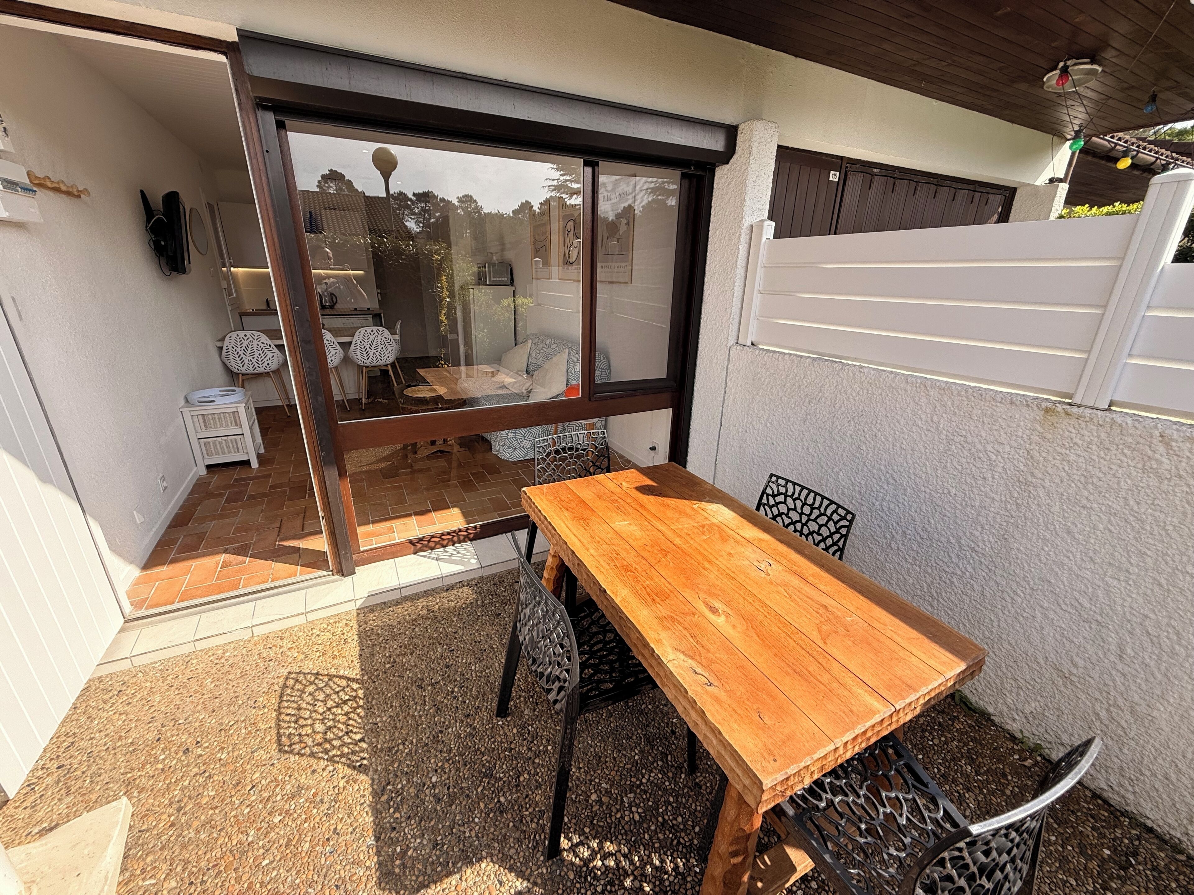 Un patio con tavolo e sedie in legno, una porta scorrevole in vetro e vista su un'area soggiorno interna.