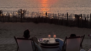 A sunset view from a beachside table with chairs, a fence, and a person in the foreground.