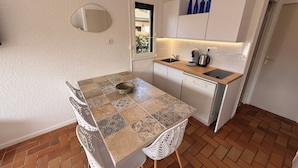 A compact kitchen with a tiled floor, a dining table with chairs, a built-in oven, and a window with a view.